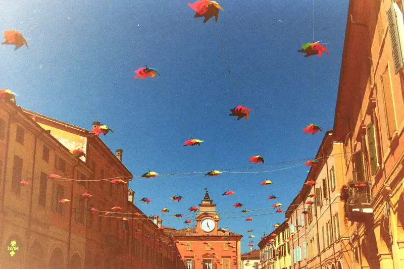 Bright kites strung across a city street beneath a blue sky.