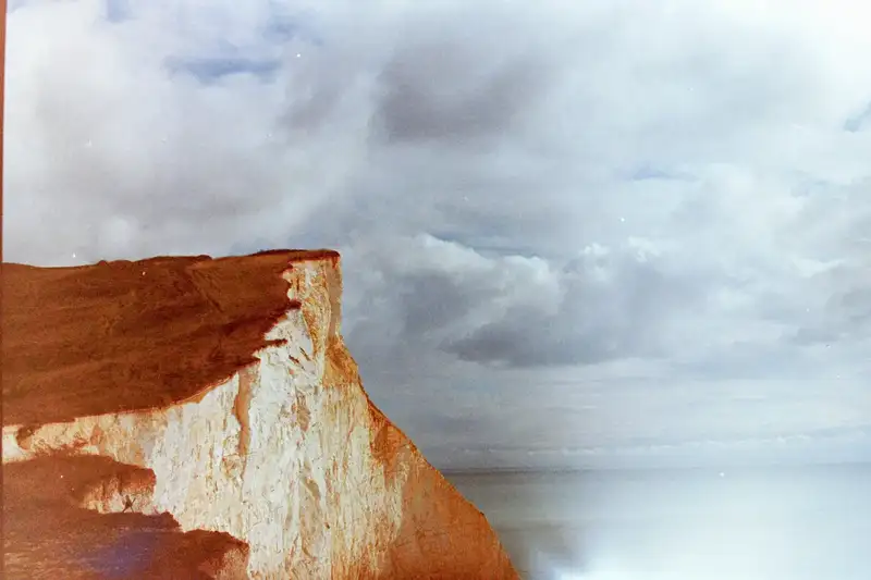 A sunlit chalk cliff meeting the sea beneath dark clouds.